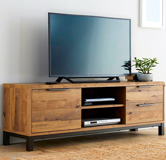 Wooden TV stand with TV standing on top and decoders on shelves, on brown jute carpet against white wall